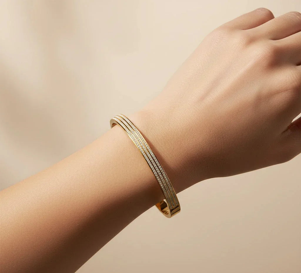 Gold bracelet on a wrist against a beige background